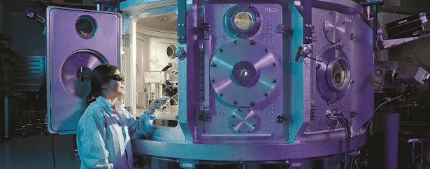 Female looking inside the door of a grey aeronautics machine dressed in a white science suit with safety goggles on pointing a science machine towards the inside.
